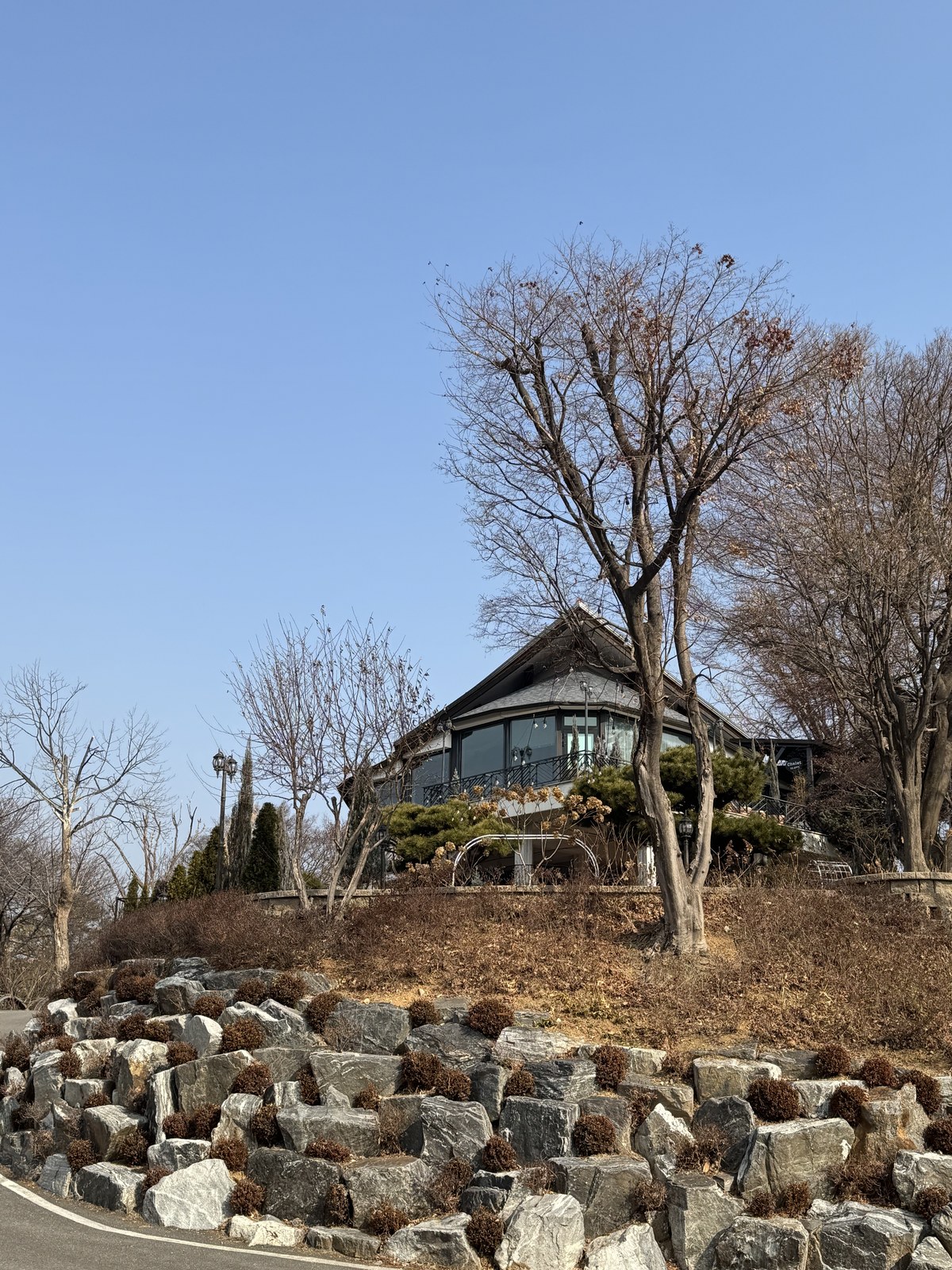 언덕 위 돌담을 두른 샬레 외관과 앙상한 겨울 나무