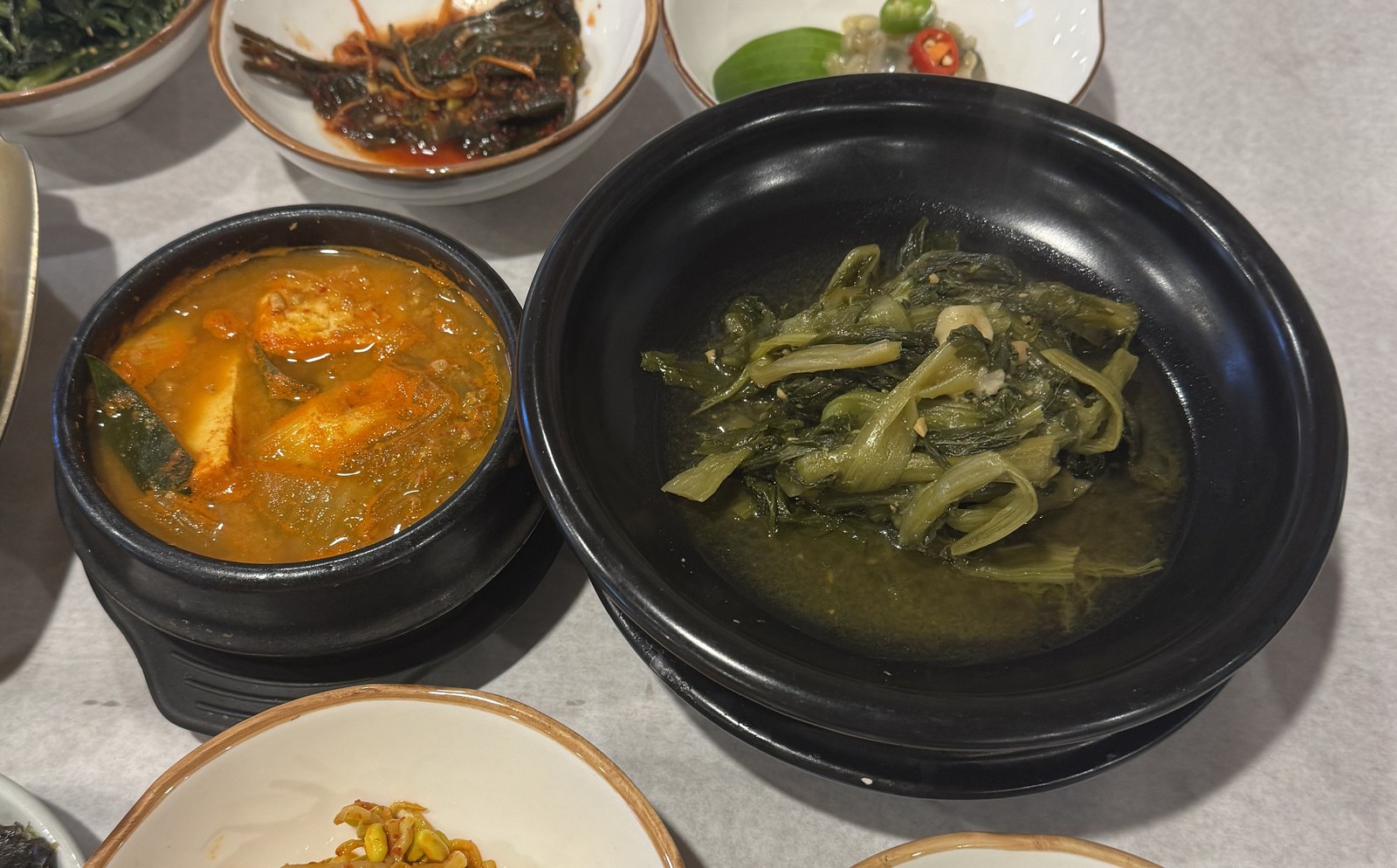 주황색 국물의 청국장 뚝배기와 시래기가 가득 담긴 검은 뚝배기