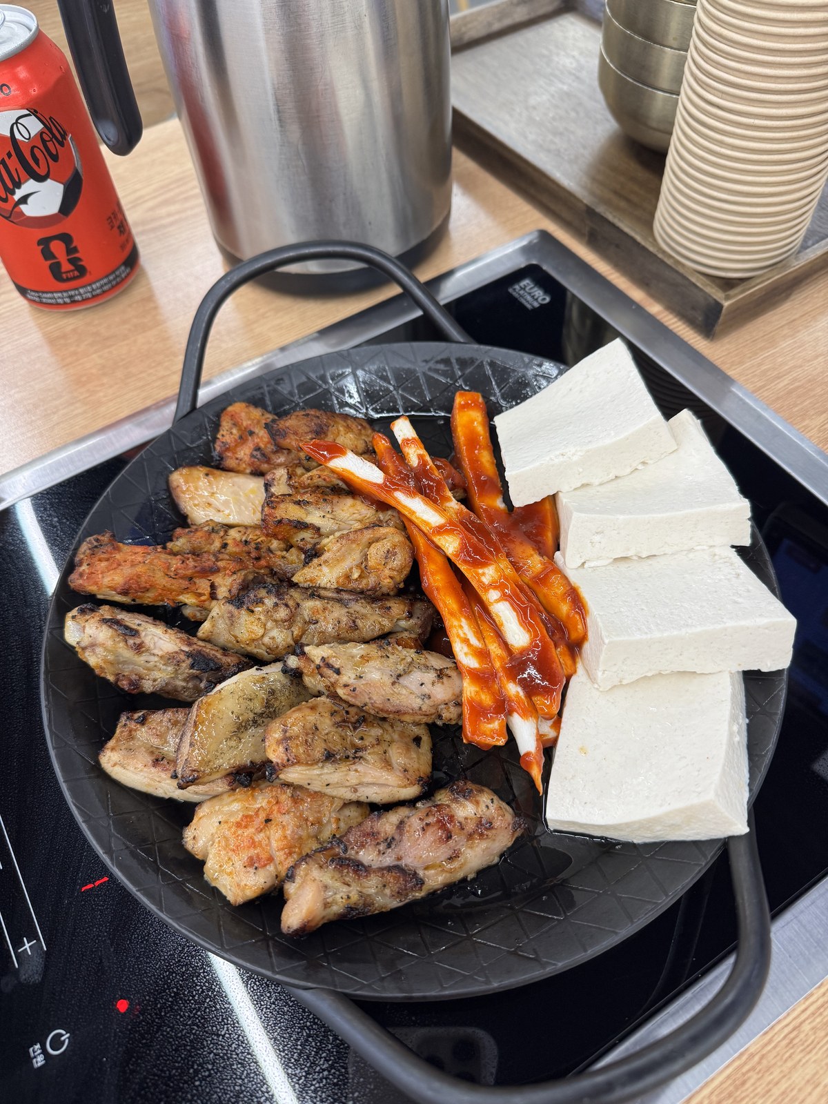 인덕션 위 판에 닭갈비와 붉은 양념 더덕, 흰 두부가 함께 올라간 모습