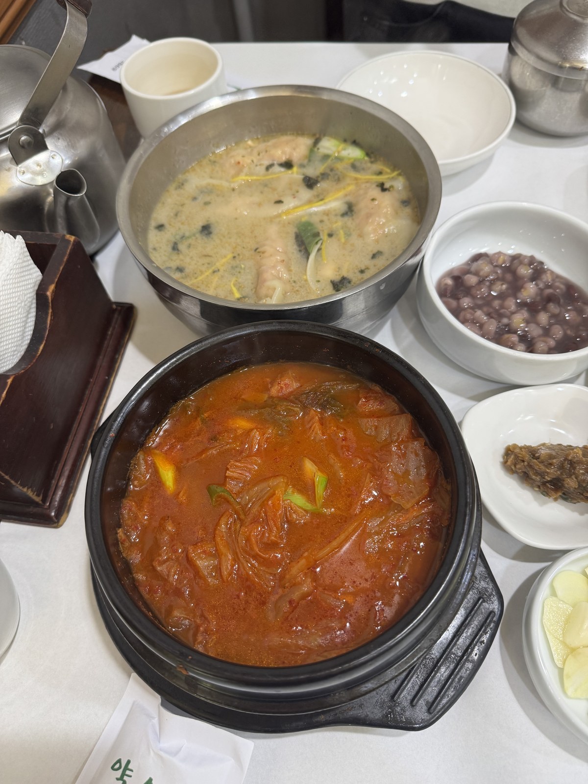 스테인리스 냄비에 담긴 뽀얀 만둣국과 얼큰한 김치찌개가 나란히 놓인 모습