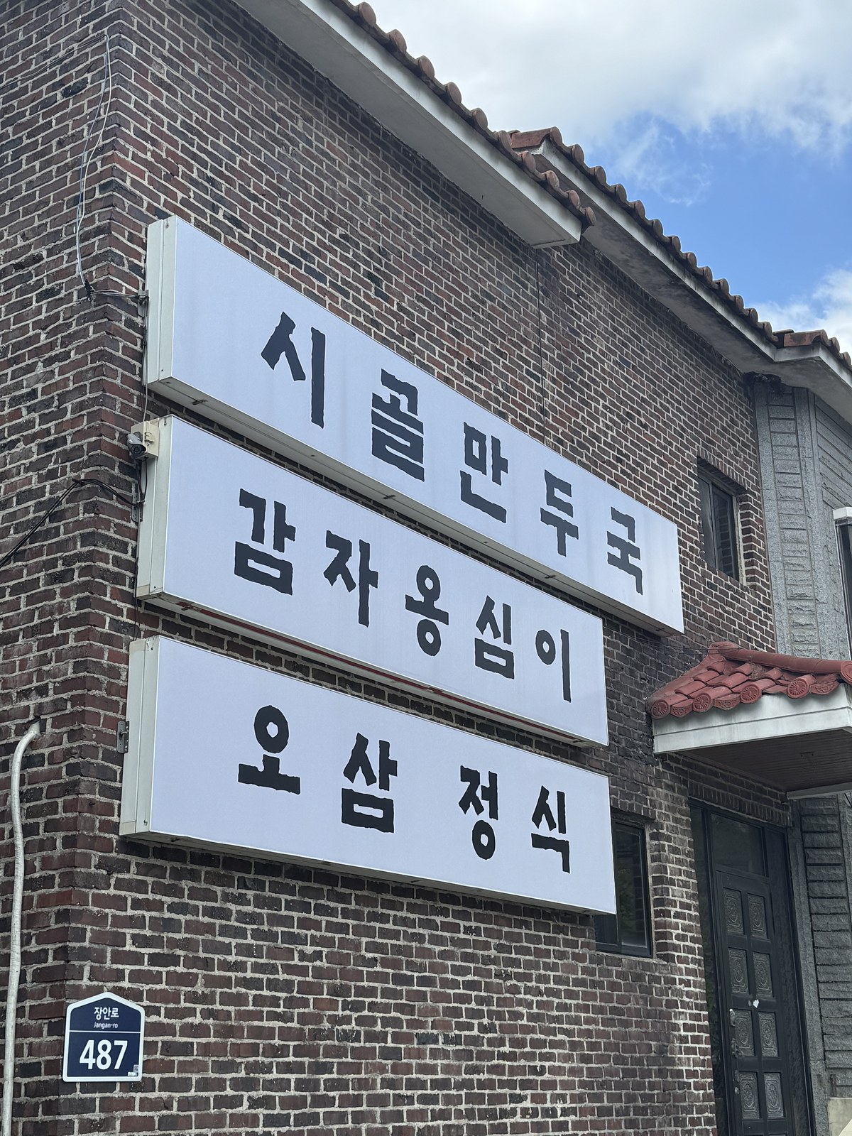 건물 벽에 걸린 시골만두국, 감자옹심이, 오삼정식 메뉴판
