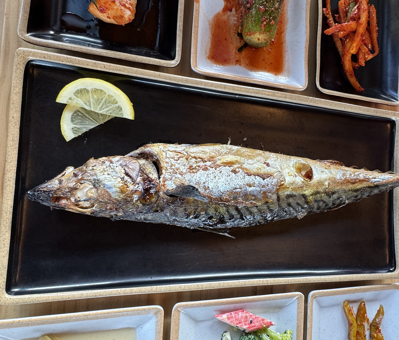 검은 접시에 가로로 누운 화덕 고등어구이 한 마리