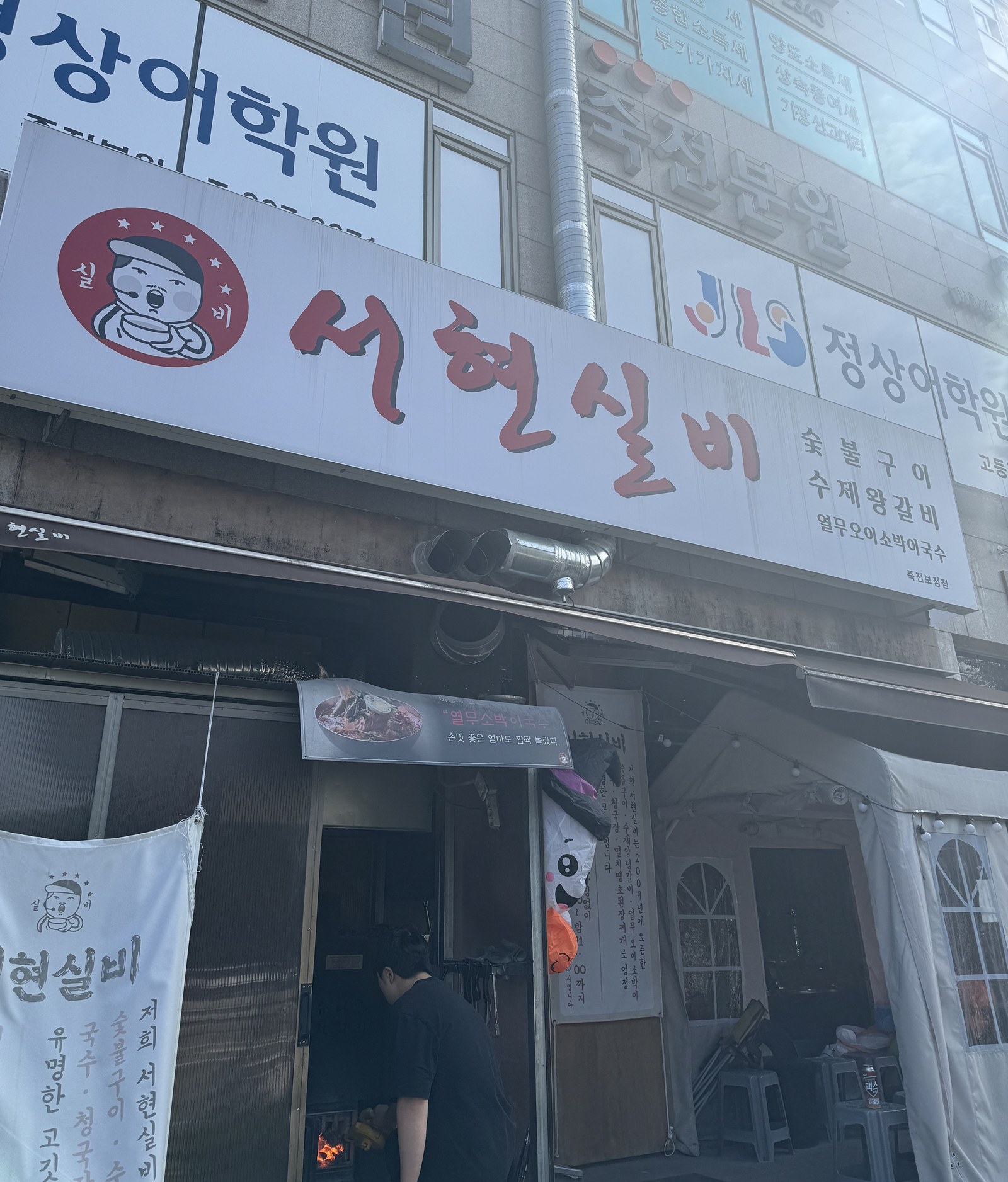 서현실비 간판 아래로 보이는 가게 입구와 문 앞에서 숯불을 피우는 모습